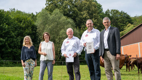 Ministerin Hinz steht gemeinsam mit Züchtern auf einer Wiese, im Hintergrund sind Rinder.