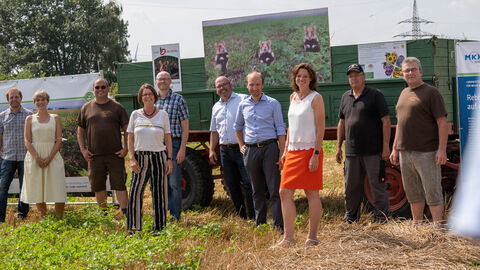 Ministerin Hinz steht gemeinsam mit Projektbeteiligten im Feld vor einem Traktor.