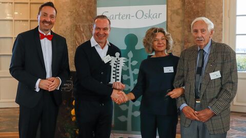 Vier Personen. Der Mann rechts in der Mitte hält einen Preis in der Hand. 