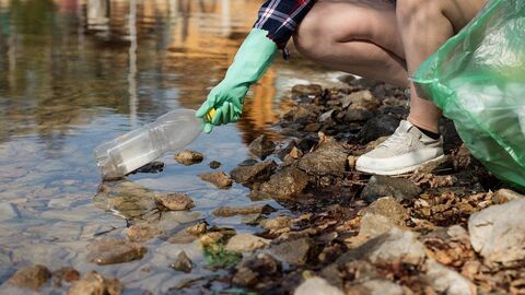 Für eine gesunde Lebensgrundlage: Unsere Umwelt gilt es zu schützen und vor Abfall und Verunreinigungen zu bewahren. Frau sammelt Plastikmüll am Fluss.