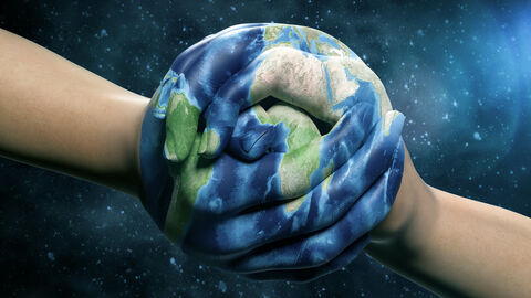 Zwei Hände halten einander fest. Auf die Hände ist die Erde gemalt.