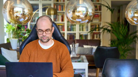 Home Office im HMUKLV Ein Mann sitzt in einem orangenen Strickpullover an einem Tisch