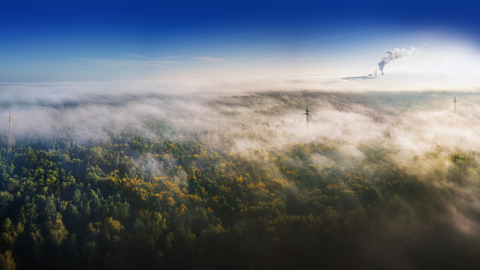 Reduktion der Treibhausgase als Klimaschutz Nebel über einem Wald und ein rauchender Fabrik Schornstein im Hintergrund