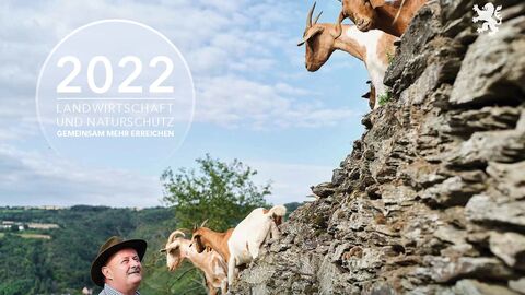 Ein Landwirt mit zwei Ziegen auf felsigen Berghängen. Ein Kreis mit dem Kalendertitl-