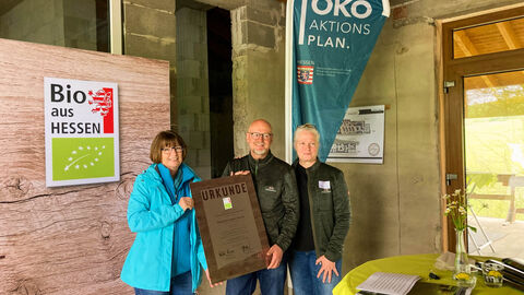 Urkundenübergabe an den Betrieb Krämer Zwei Frauen und ein Mann halten eine große Urkunde in der Hand