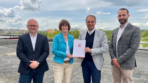 Drei Männer und eine Frau stehen zusammen. Die Frau hält einen Bescheid in der Hand