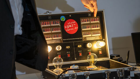 Stromcheck zu Hause Ein Koffer aufgeklappt auf einem Tisch, darin leuchten Glühbirnen