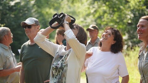 Ministerin Hinz schaut durch ein Fernglas in die Baumkronen.