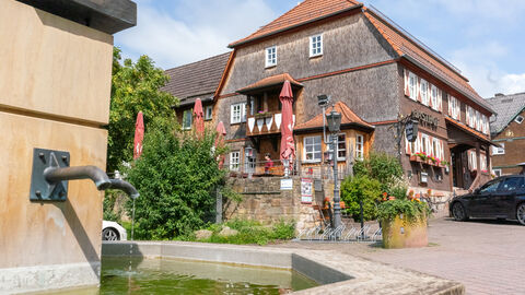 Ein Gasthof mit Brunnen im Vordergrund