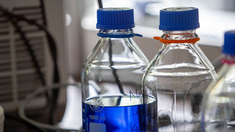 Glasflaschen in einem Labor. Eine Flasche ist mit blauer Flüssigkeit gefüllt