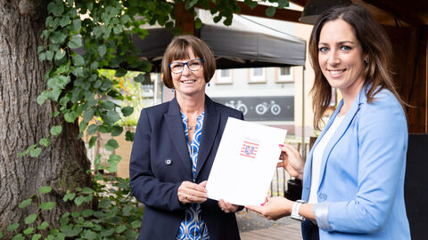 Zwei Personen (w) halten einen Förderbescheid mit Hessen Wappen