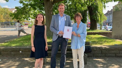 Ministerin Priska Hinz mit Kassels Oberbürgermeister Dr. Sven Schoeller und Klimaanpassungsmanagerin Katharina Nießner Drei Personen im Freien bei der Bescheidübergabe