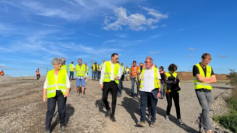Personengruppe mit Warnwesten gehen über Schotterähnliche Fläche.