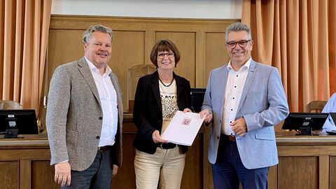 Drei Personen (m/w/m) in einem Saal mit Förderbescheid in der Hand.