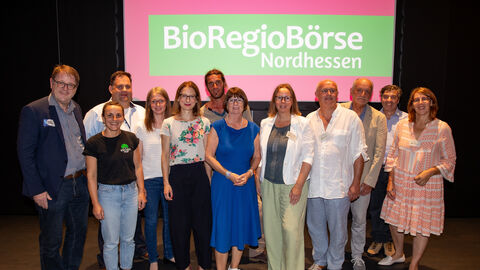 Thomas Ackermann (Dezernent Umwelt- und Naturschutz Landkreis Kassel), Sophia Seidl (Eschenhof Vermarktung), Andreas Althoff (Ökomodell-Region Waldeck-Frankenberg), Juliane Wagener (Ökomodell-Region Schwalm-Eder-Kreis), Nicole Maisch (Schuldezernentin Stadt Kassel), Moritz Wintzer-Brand (Solawi Falkenhof GbR), Priska Hinz (Hessische Umweltministerin), Daniela Schwarz (Ökomodell-Region Nordhessen), Frank Neumann (Ökomodell-Region Hersfeld-Rotenburg), Jürgen Heß (Zentrum für ökologische Landwirtschaft), Stefan Itter (Ökomodell-Region  Schwalm-Eder-Kreis), Silke Flörke (Ökomodell-Region Nordhessen). Viele Personen mit Ministerin Hinz auf der BioRegioBörse in Kassel.