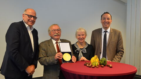 Ehrung für Manfred Guder Drei Männer und eine Frau stehen an einem Stehtisch. Einer der Männer hält eine goldene Plakette in der Hand.