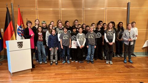 Eine Frau und viele Jungen und Mädchen stehen vor einer Holzwand