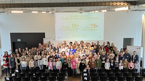 Mehrere Schülerinnen und Schüler stehen in einer Aula