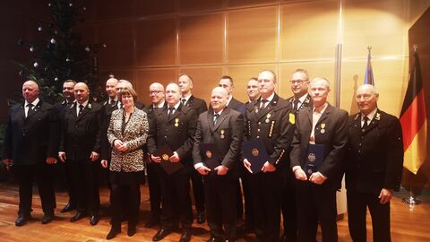 Eine Gruppe von Männern in schwarzen Anzügen und eine Frau stehen vor einer Holzwand