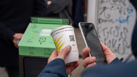 Person scannt mit Smartphone den QR-Code des Bechers.
