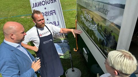 Landwirtschaftsminister Jung steht beim Festival „Blues, Schmus, Apfelmus“ an einem Stand mit regionalen Fischspezialitäten.