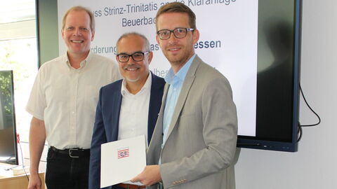 Drei Personen. Rechts Staatssekretär Michael Ruhl bei der Übergabe des Förderbescheids.