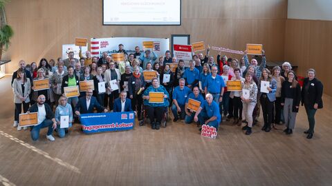 Viele Menschen mit Ortsschildern und Plakat "Engagement-Lotsen".