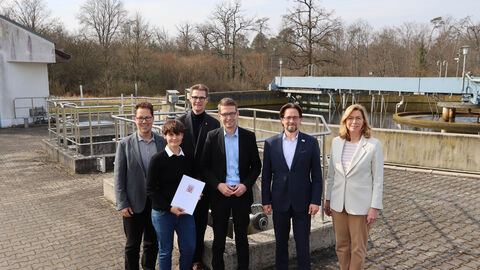 Fünf Personen (w+m) mit einem Bescheid lächeln in die Kamera.