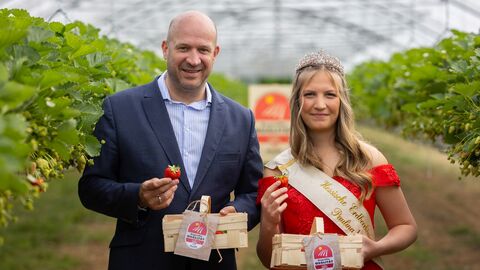Minister Jung und Erdbeerkönigin Paulina halten Erdbeeren hoch