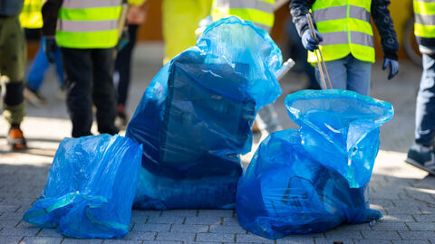 Bei beiden Aktionstagen waren hessenweit viele Kinder im Einsatz, um Müll zu sammeln. Volle Mülltüten, im Hintergrund Kinder beim Müllaufsammeln.