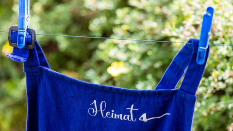 Eine Schürze mit Aufdruck "Heimat" hängt an einer Wäscheleine