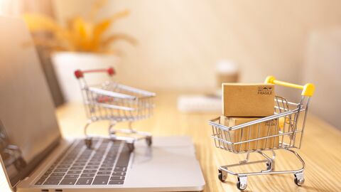 Ein Laptop und ein kleiner, befüllter Einkaufswagen stehen auf einem Schreibtisch.