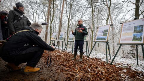 Hessens Forstminister Ingmar Jung spricht vor Journalisten im Wald, hinter ihm sind Schautafeln aufgestellt.